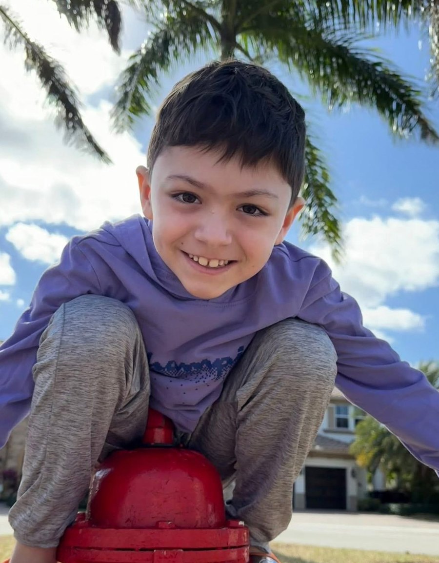 Finn, smiling, perched on a red fire hydrant under palm trees